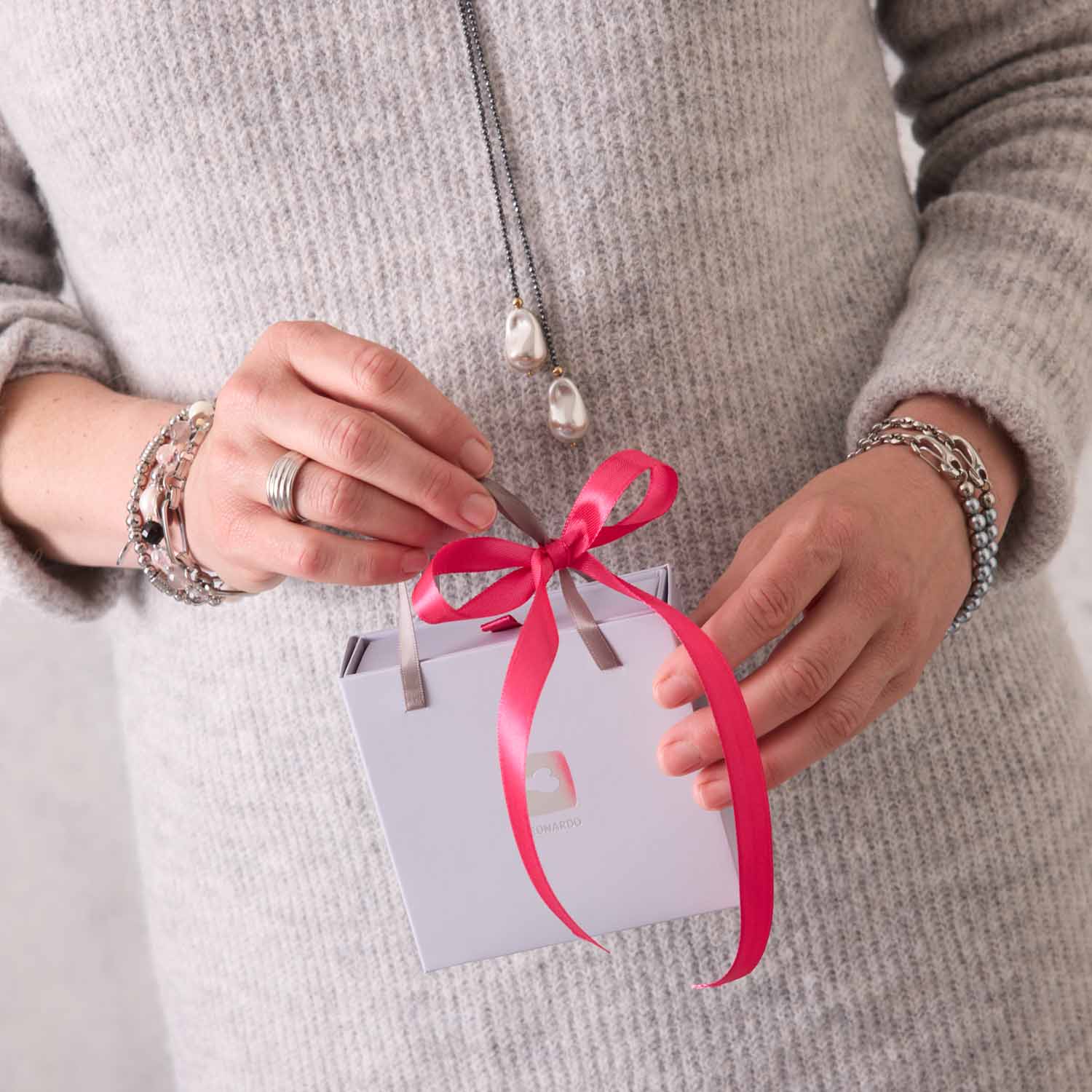 Frau haelt Armband MATHILDE Clip & Mix in silber mit rosa Schleife und Geschenkverpackung