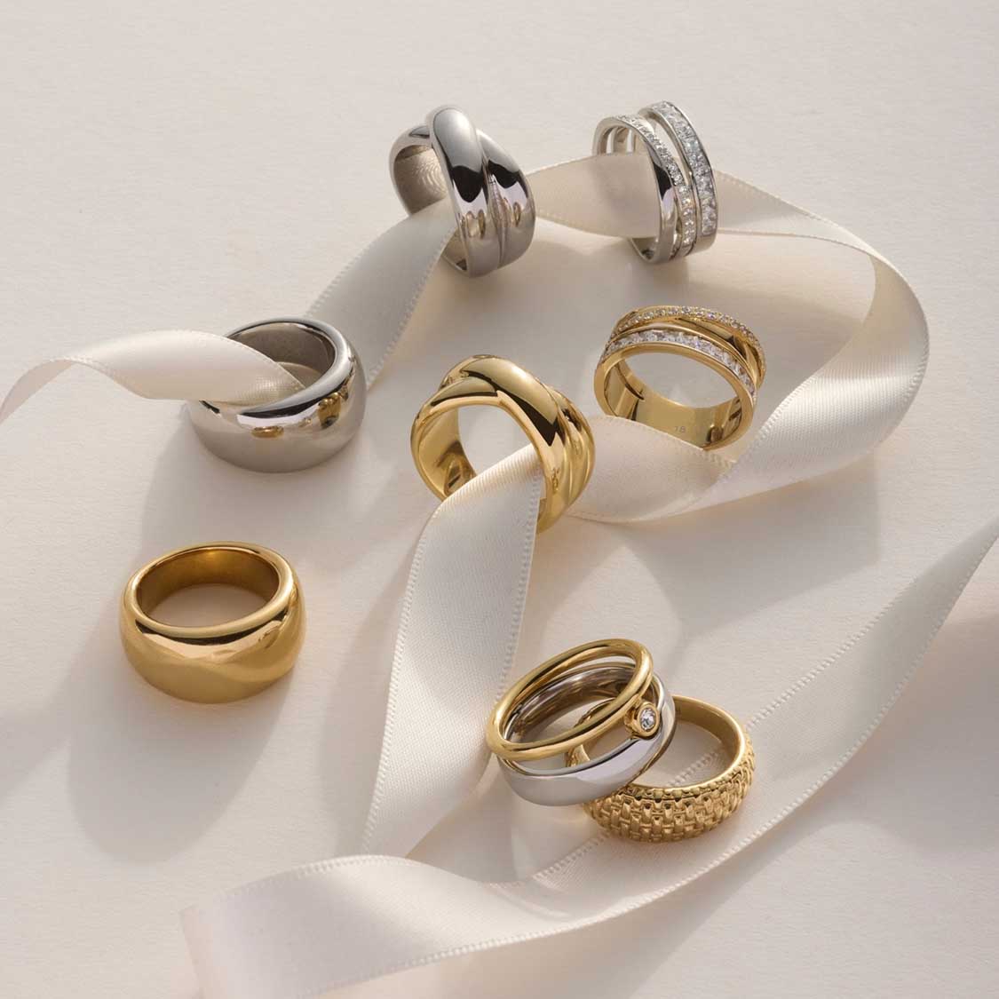 Mehrere Ringe in Gold- und Silbertönen auf weißem Satinband arrangiert