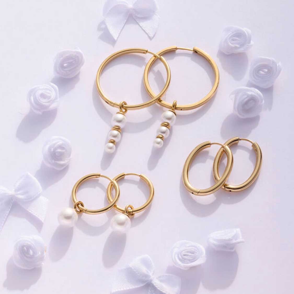 Creolen LUZIE gold mit Perlen, umgeben von weißen Rosen auf weißem Untergrund