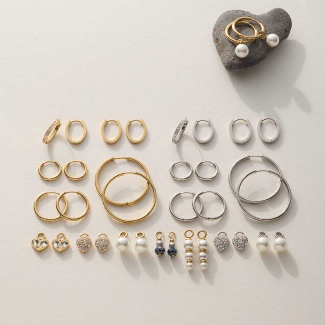 Schmuckkollektion mit goldenen und silbernen Ringen, Ohrringen und Perlenanhängern auf weißem Untergrund