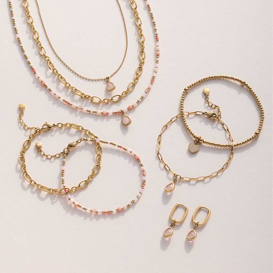 Mehrere goldene Armbänder und Ohrringe in Kettenoptik mit rosafarbenen Perlendetails
