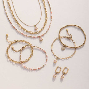 Mehrere goldene Armbänder und Ohrringe in Kettenoptik mit rosafarbenen Perlendetails