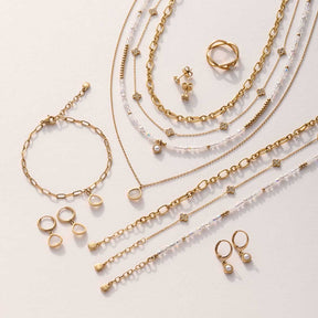 Schmuckkollektion mit Armbändern, Halsketten, Ringen und Ohrringen in Gold und Weiß auf hellem Untergrund