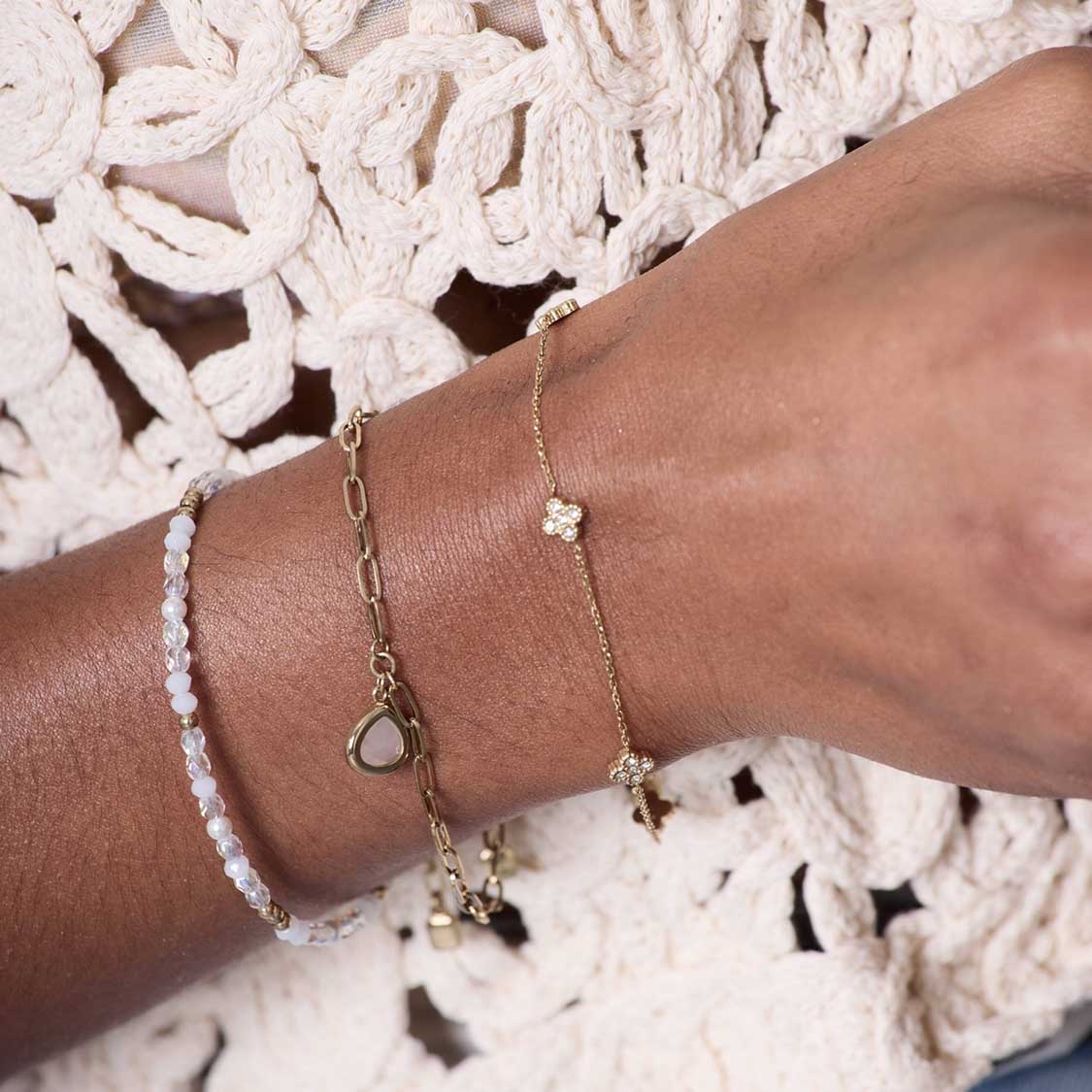 Armband INDRA gold CIAO an Frauenhand getragen, mit weißem Spitzenarmband kombiniert