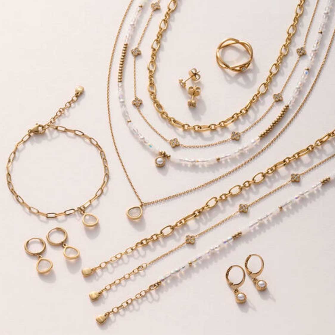 Goldene Ohrringe, Ringe, Ketten und Armbänder aus der Serie INDRA auf hellem Hintergrund