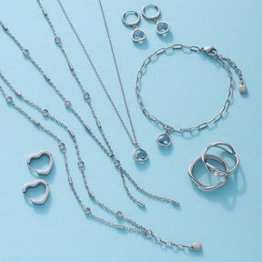 Silberfarbene Schmuckkollektion mit Halsketten, Ringen, Armbändern und Ohrringen auf hellblauem Hintergrund