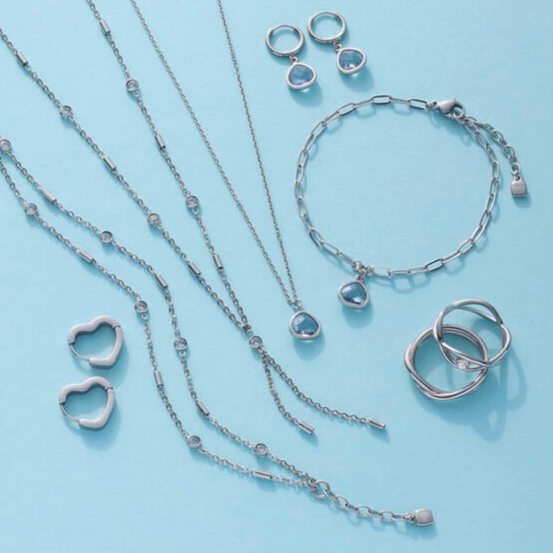 Schmuckkollektion aus Halsketten, Ringen und Ohrringen auf hellblauem Hintergrund