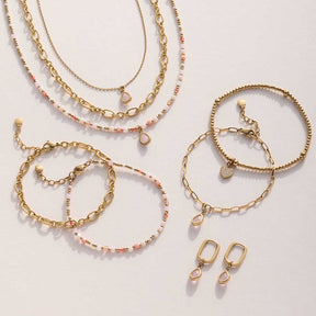 Schmuck-Set aus Halsketten, Armbändern und Ohrringen in Gold und Rosa auf hellem Untergrund