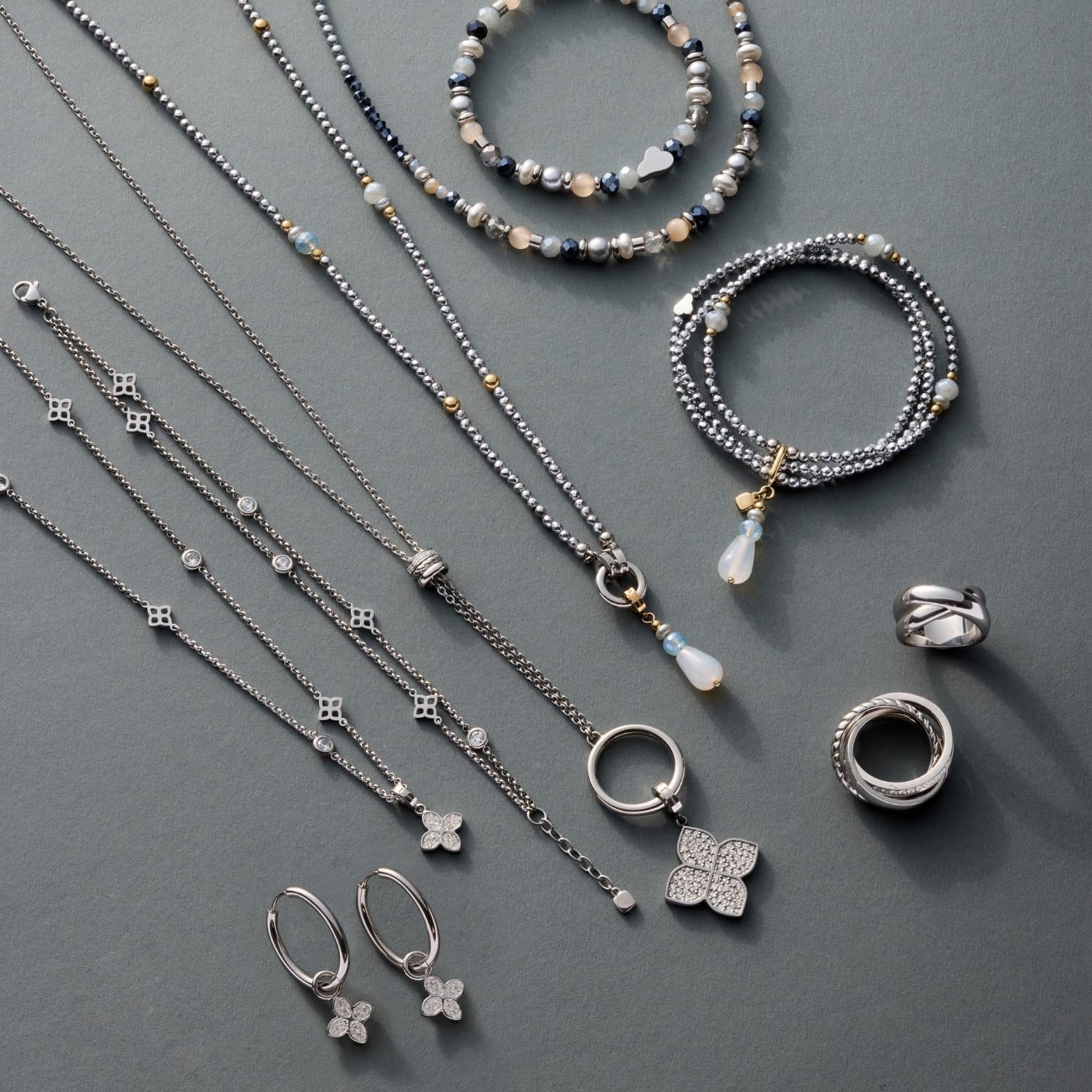 Silberne Halsketten, Armbänder und Ohrringe mit Perlen und Anhängern auf grauem Untergrund