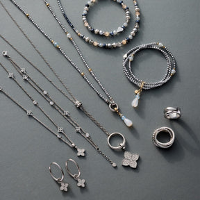 Silberne Halsketten, Armbänder und Ohrringe mit Perlen und Anhängern auf grauem Untergrund