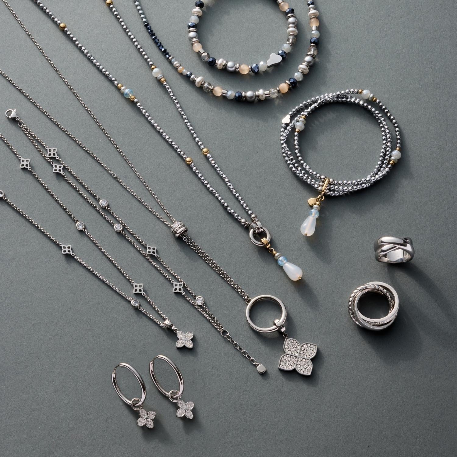 Silberner Schmuck auf grauem Untergrund: Armbänder, Halsketten, Ringe und Ohrringe