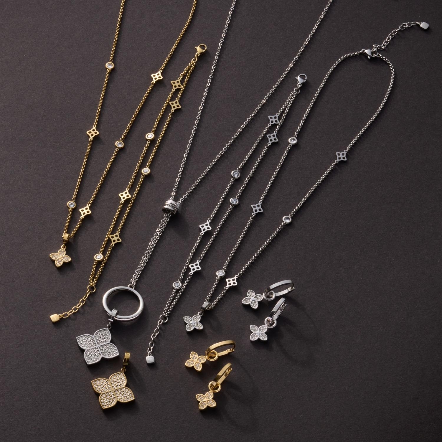Goldene und silberne Halsketten sowie Ohrringe und Ringe mit Ziersteinen auf grauem Hintergrund