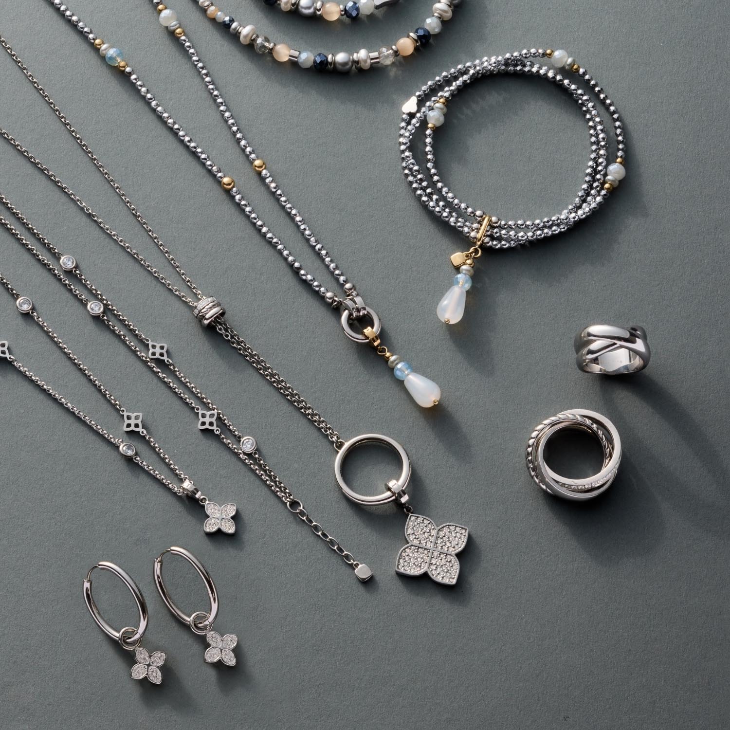 Schmuckkollektion mit Halsketten, Ringen, Ohrringen und Armbändern aus Silber auf grauem Untergrund