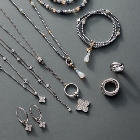 Schmuckkollektion mit Halsketten, Ringen, Ohrringen und Armbändern aus Silber auf grauem Untergrund