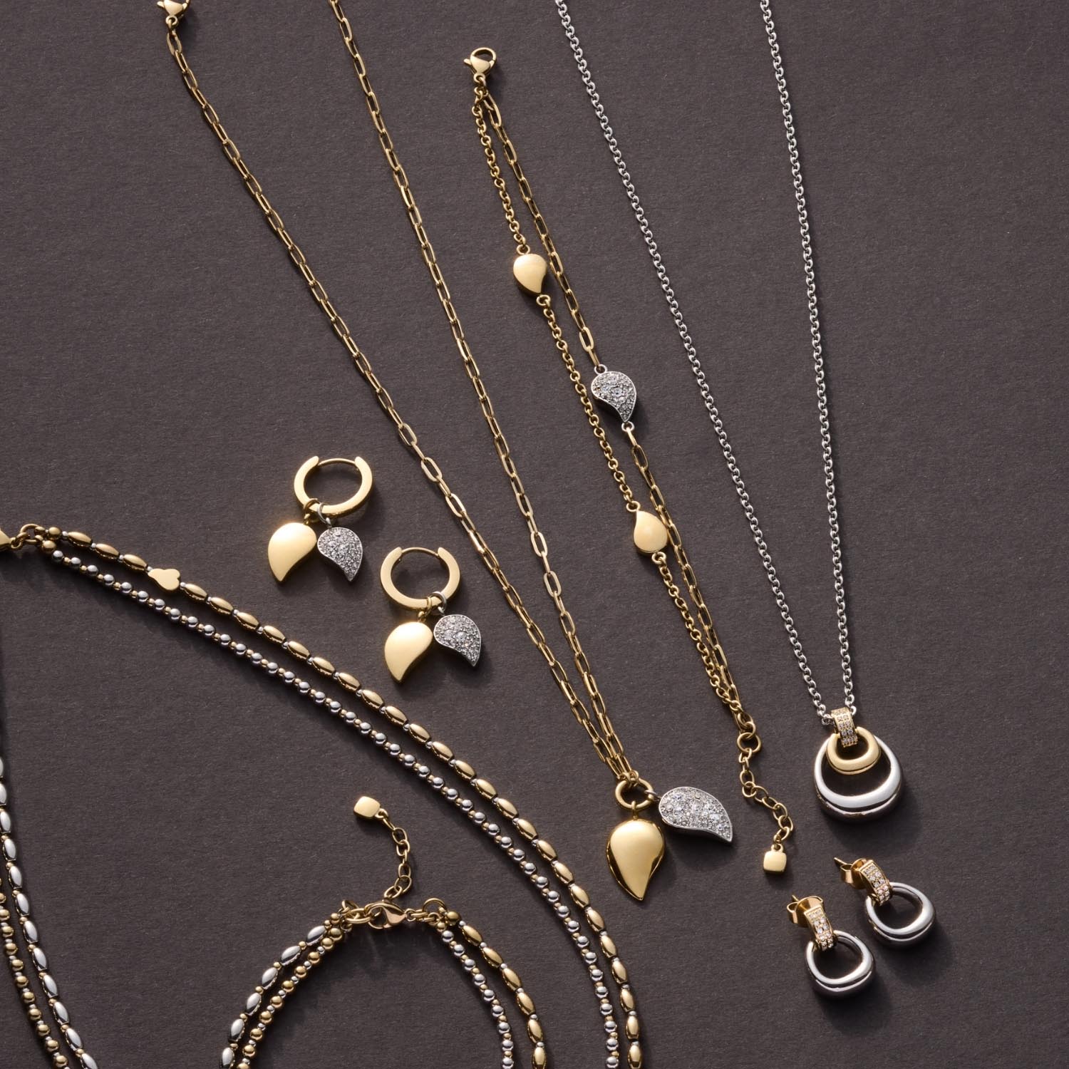 Schmuckkollektion mit Ketten, Ohrringen und Armband in Edelstahl bicolor auf grauem Hintergrund