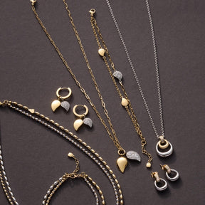 Schmuckkollektion mit Ketten, Ohrringen und Armband in Edelstahl bicolor auf grauem Hintergrund