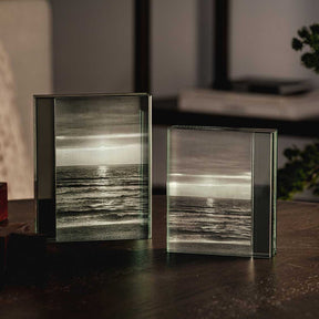 Zwei Bilderrahmen LINEA aus Glas auf dunklem Tisch mit Meerlandschaft, Wohnraum im Hintergrund