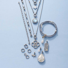 Armband NOURA Clip & Mix mit Schmuckcharms und Kettenanhängern auf hellblauem Untergrund