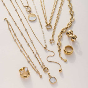 Goldene Ketten und Armbänder mit austauschbaren Clip-Anhängern, Ringe und Perlenelemente auf weißem Hintergrund