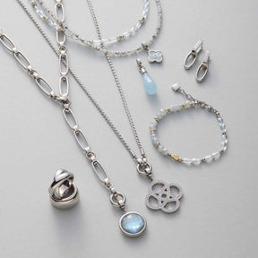 Silberne Schmuckkollektion mit Halskette, Armband, Ring und Ohrstecker auf grauem Hintergrund