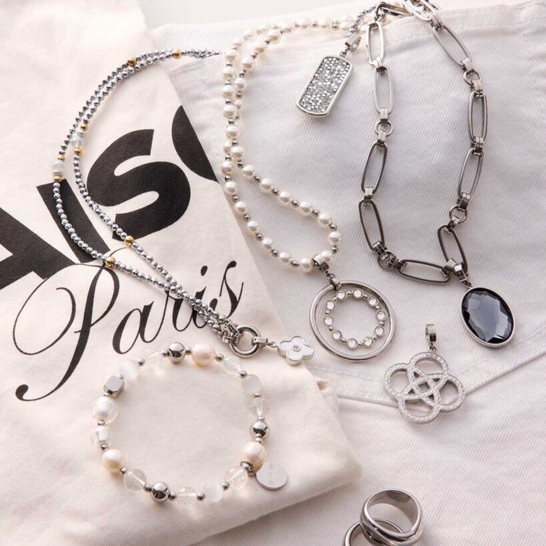 Mehrere Silberschmuck-Ketten und Anhänger BLEUR Clip & Mix auf Papier mit Paris-Motiv arrangiert