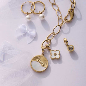 Anhänger SOLARIS gold mit Kette, Ohrringen und weißen Schleifen-Charms auf weißem Hintergrund