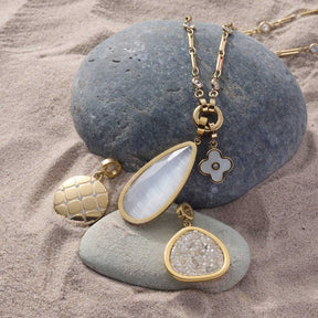 Anhänger BLUNA gold Clip & Mix auf Steinen am Strand, verschiedene Charms mit Edelsteinen
