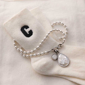Silberner Perlenarmband mit Anhängern auf weißer Socke mit Buchstabe G