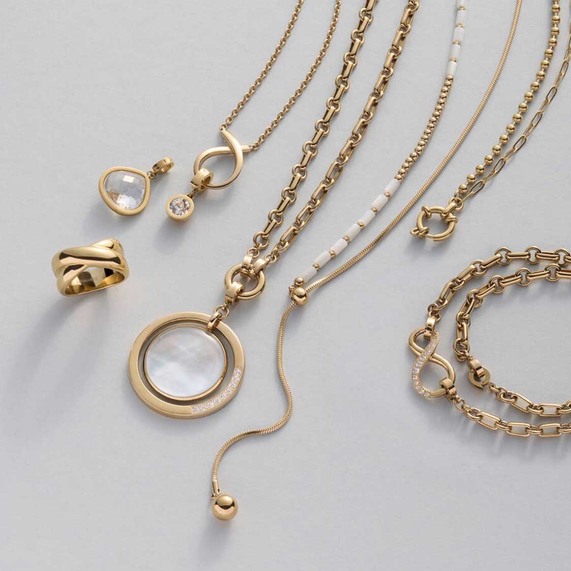 Goldene Schmuckkette mit Edelstahlring und verschiedenen Kettenanhängern auf Grau