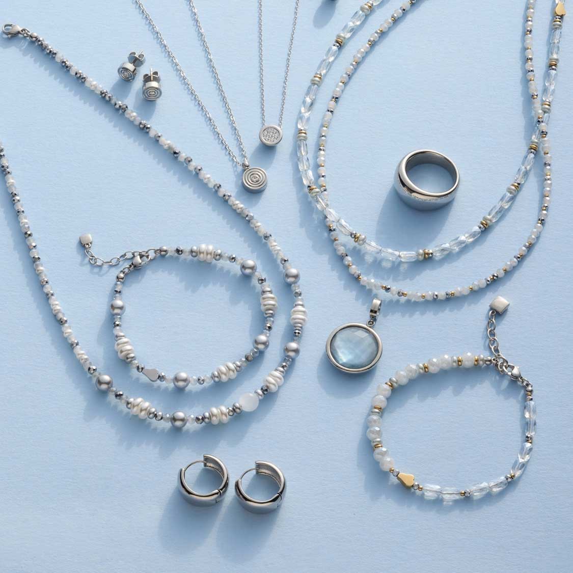 Silberne Halsketten, Armbänder und Ringe mit Perlen und Anhängern auf hellblauem Hintergrund