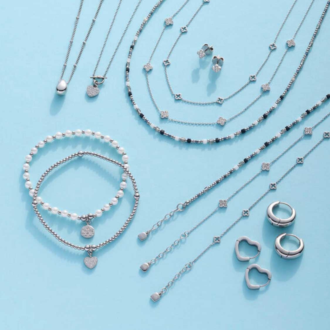 Silberner Schmuck der Serie LUVELLA auf hellblauem Hintergrund: Creolen, Ketten, Armbänder und Ohrringe