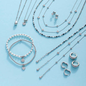 Silberner Schmuck der Serie LUVELLA auf hellblauem Hintergrund: Creolen, Ketten, Armbänder und Ohrringe