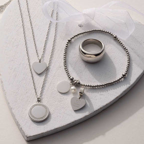 Armband DEBBY silber mit Perle und Herzanhängern auf weißem Tablett, zusammen mit Ring und Halsketten