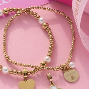 Armband DEBBY gold mit Perlen und goldfarbenen Charms auf rosa Untergrund