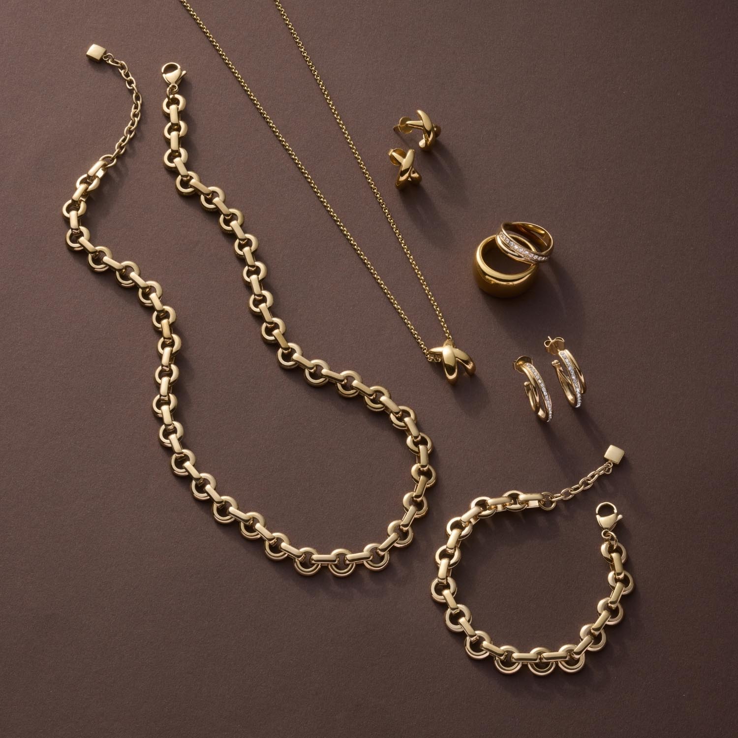Halskette SOPHIE, Armband und Ringe aus Gold auf braunem Hintergrund