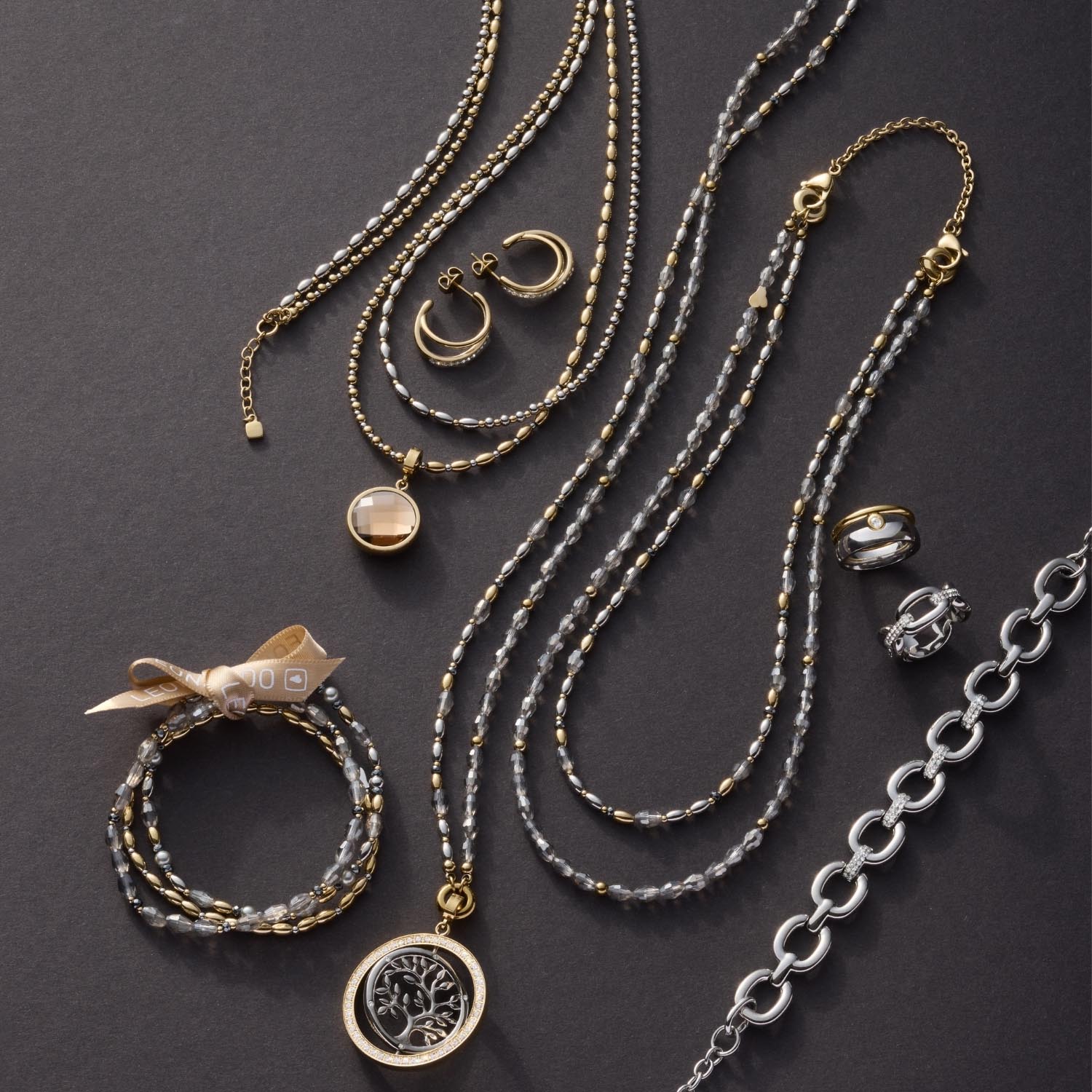 Schmuckkollektion mit Halsketten, Armbändern und Ohrringen in Gold und Silber auf grauem Untergrund