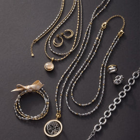 Schmuckkollektion mit Halsketten, Armbändern und Ohrringen in Gold und Silber auf grauem Untergrund