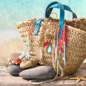 Halskette SOLERA mit Glasperlen neben Strohtasche am Strand