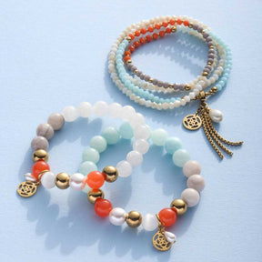 Mehrere Glasperlen-Armbänder in Blau-, Weiß- und Orangetönen mit goldenen Metallperlen und Anhängern auf hellem Hintergrund
