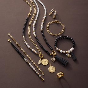 Schmuckset mit Halsketten, Armbändern und Ohrringen in Gold und Schwarz auf neutralem Hintergrund