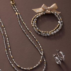 Armband AGNETA mit Glasperlenkette, Schleife und passenden Ohrringen auf braunem Hintergrund