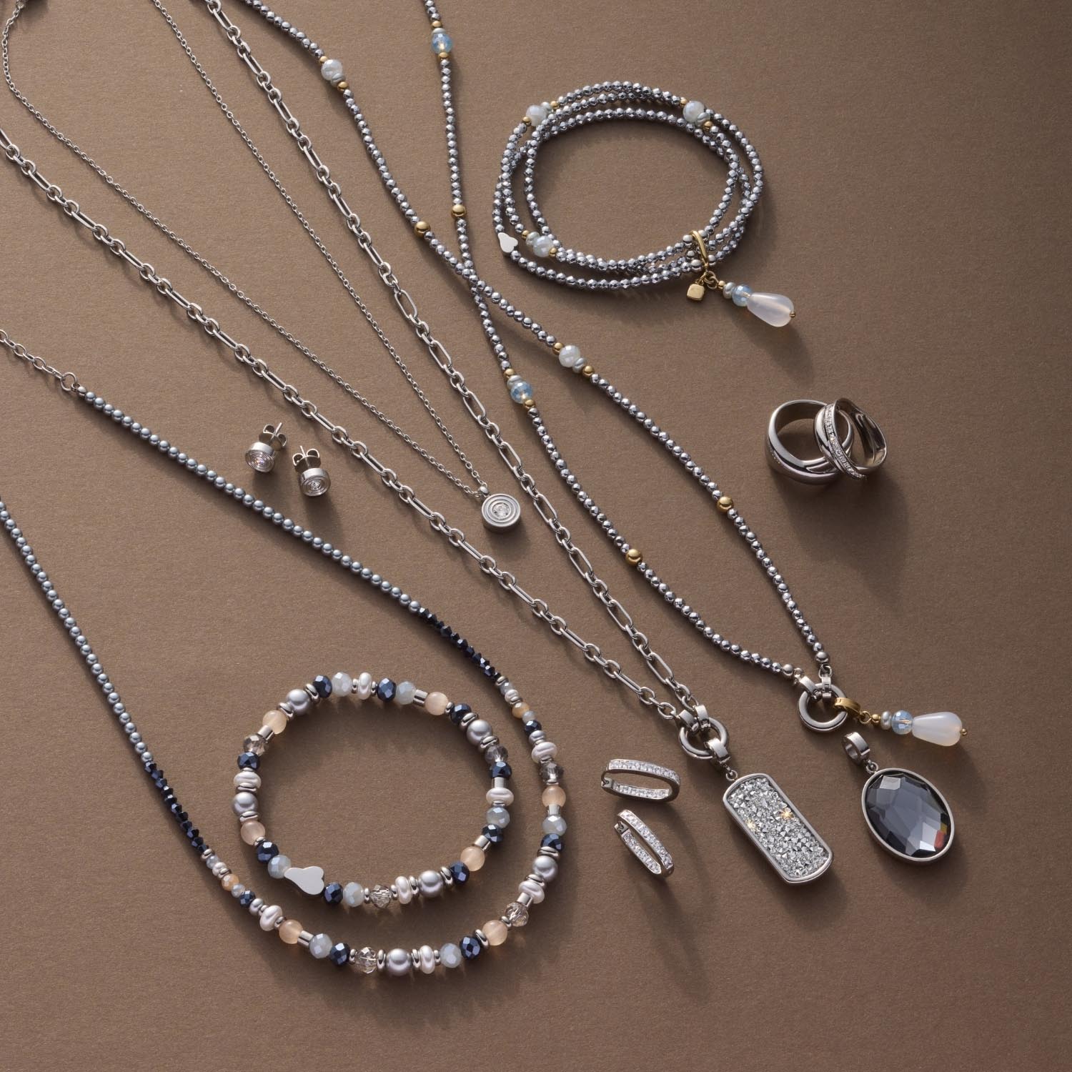 Silberne Halsketten, Armbänder und Ringe aus Glas auf beigem Hintergrund arrangiert