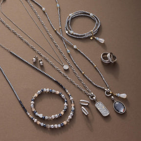 Silberne Halsketten, Armbänder und Ringe aus Glas auf beigem Hintergrund arrangiert