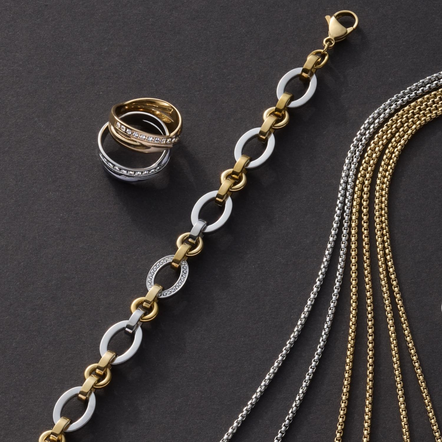 Ring DARIA 18, Armbänder und Ketten in Gold und Silber auf grauem Hintergrund