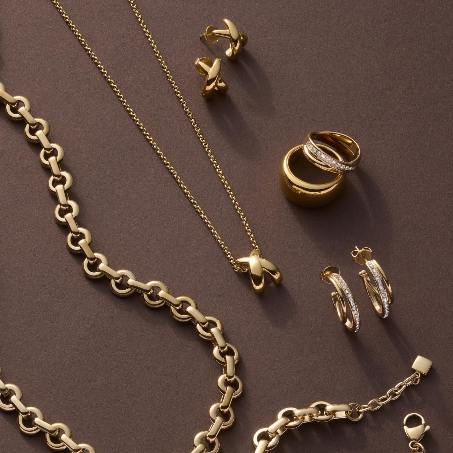 Goldschmuck-Kollektion mit Ring DARIA 17, Ketten und Ohrringen auf grauem Untergrund