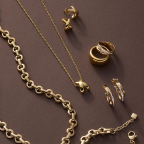 Goldschmuck-Kollektion mit Ring DARIA 17, Ketten und Ohrringen auf grauem Untergrund
