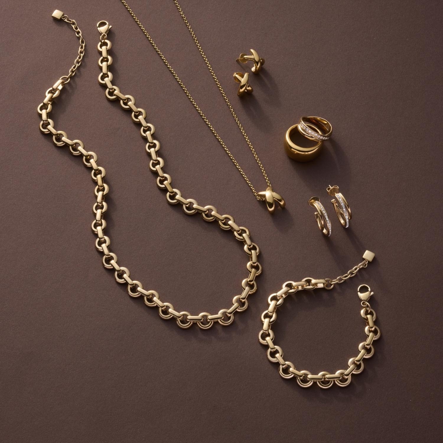 Goldene Schmuckkollektion mit Armband NALA, Kette, Ringen und Ohrringen auf grauem Hintergrund