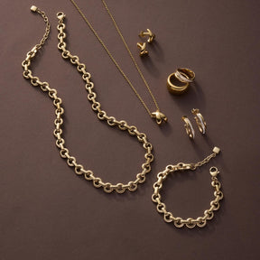 Goldene Schmuckkollektion mit Armband NALA, Kette, Ringen und Ohrringen auf grauem Hintergrund