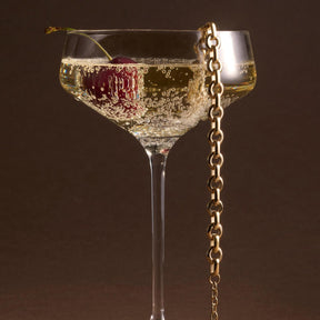 Armband NALA in Gold neben Champagnerglas mit Perlen
