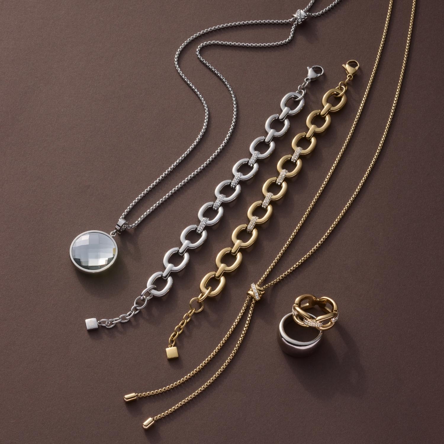 Armband BELLE gold mit Gliederkette, daneben Halsketten und Ring in Gold- und Silbertönen auf braunem Hintergrund